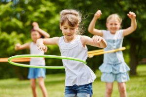 3 Kinder spielen mit Hula Reifen auf der Wiese.