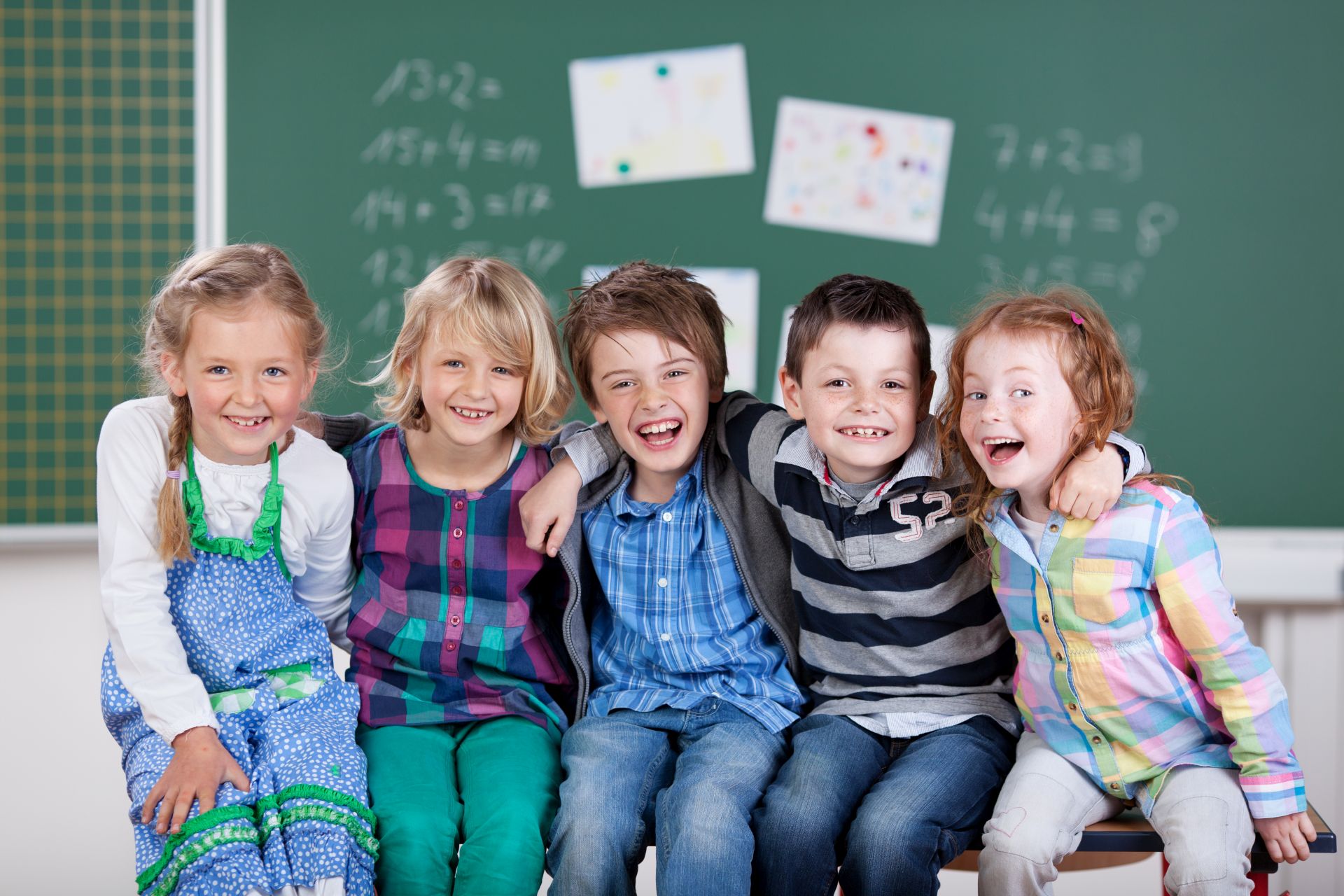Gruppe von Kindern, die vor der Tafel sitzen und lachen.