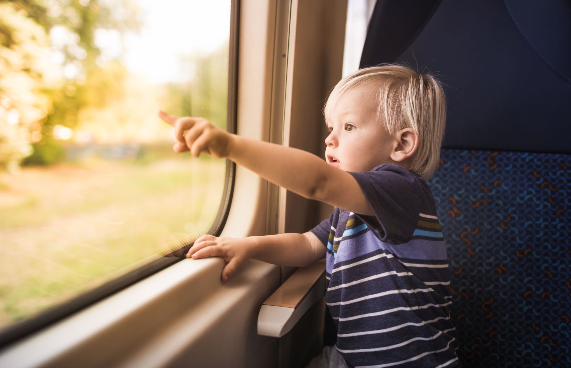 Kleiner Junge sitzt im Zug am Fenster und zeigt mit Finger aus dem Fenster.