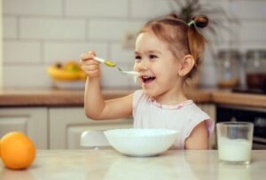 Kleines Maedchen isst Joghurt und lacht dabei.
