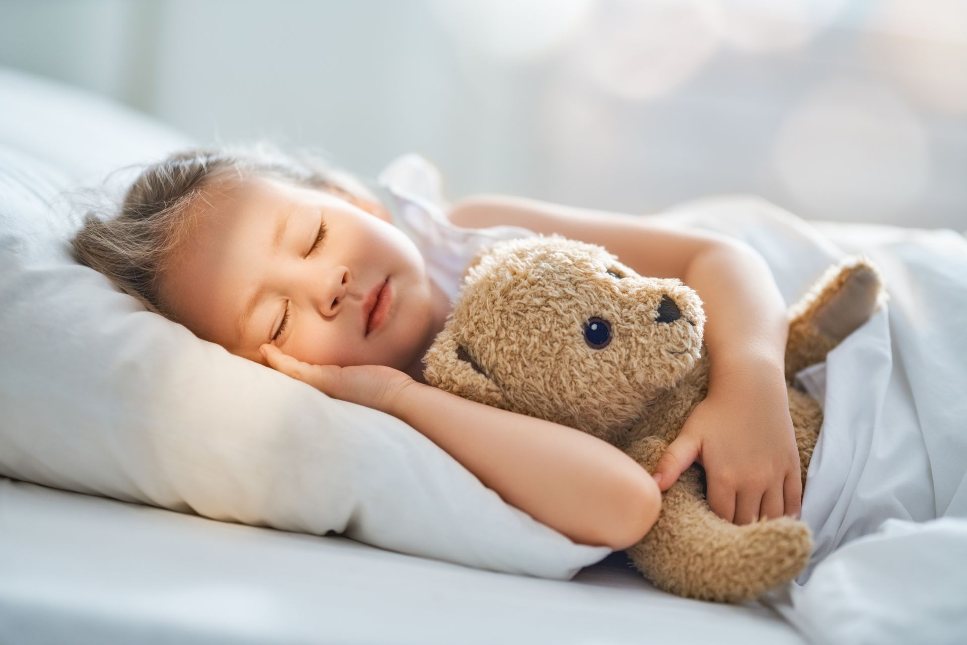 Kleines Maedchen schlaeft mit Teddy im Arm.