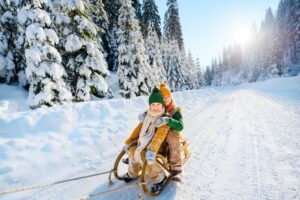 Zwei Kinder mit Schlitten im Schnee.
